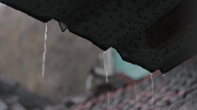 Water droplets dripping from an eave onto a pile of gravel