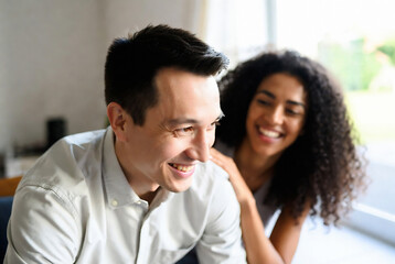 Obraz premium A man and a woman are smiling at each other, enjoying a moment together in a bright room with a window view.