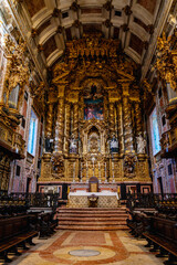 Obraz premium View inside Porto Cathedral showing central nave with stone arches wooden benches and ornate golden altar. Historic religious architecture with visitors sitting in quiet atmosphere.