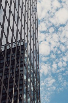 Urban architecture shows a vertical glass office facade and reflection while sky clouds provide bright copyspace for layout design