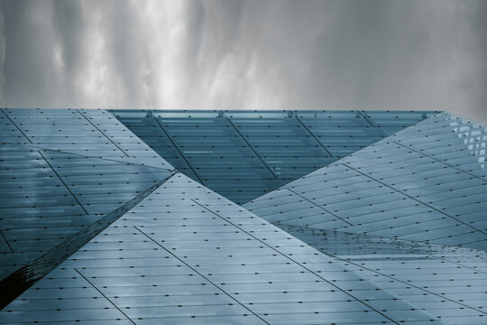 Modern urban architecture facade shows geometric metallic abstract forms against sky clouds with generous copyspace and negative space for text