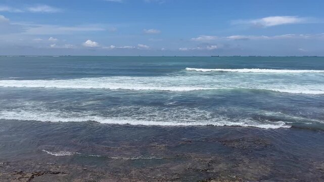 Calm seascape under blue sky, waves gently rolling towards the shore. Romantic oceanic background without people with empty space for credits.