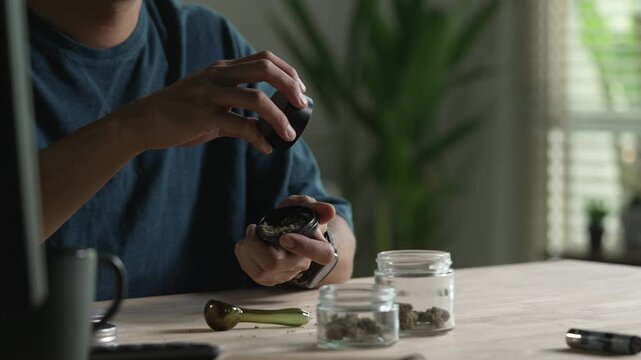 Man using cannabis grinder, with cannabis equipment and accessories on the table.