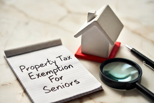 A note about a property tax exemption for seniors is displayed with a miniature house, magnifying glass, and pen on a wooden surface.