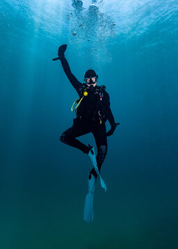 A scuba diver having fun underwater, doing a funny dance pose on the safety stop in mid-water