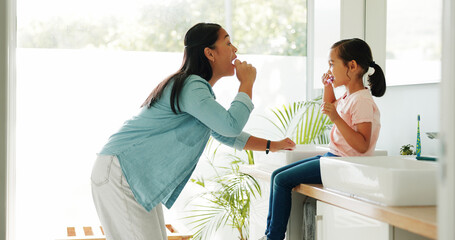 Obraz premium Mother, girl and brushing teeth in bathroom for learning, oral hygiene and morning routine for bonding. Teaching, woman and child with toothbrush for dental care, cleaning mouth demonstration or home