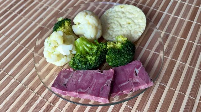 Light breakfast on glass plate broccoli. Boiled cauliflower paired with round rice white bread and two slices pork tongue.