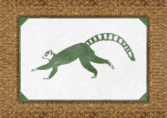 Vintage ring-tailed lemur illustration in green ink on textured paper with decorative border, placed on woven straw background. Minimalist safari-style animal poster. © Lisa