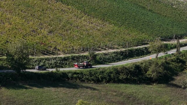 Tractor and SUV moving along rural road between vineyard rows in Colli Piacentini Martani near Piacenza Emilia Romagna Italy within Val d Arda viticulture landscape, drone orbit shot