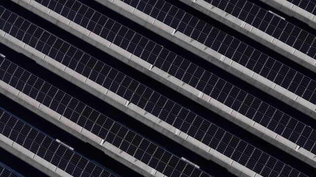 Photovoltaic solar panels on industrial rooftop in Po Valley arranged in parallel arrays producing renewable electricity, top down drone panning shot
