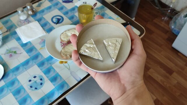Person holding foil-wrapped processed cheese triangles in hand, at kitchen, first person view