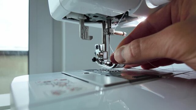 Close up of man threading needle on sewing machine before stitching. Tailoring preparation, machine setup and textile craft concept.