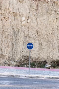 Urban roadway sign near sidewalk and curb on street guides traffic direction and circulation with wall backdrop for safe city movement
