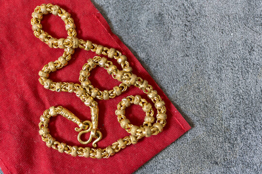 A beautifully crafted Thai gold necklace is placed on a red velvet bag