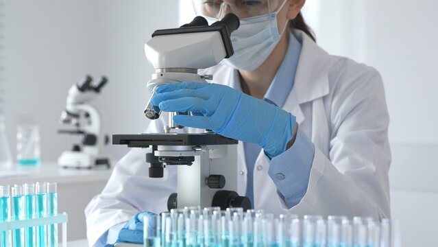 A scientist in protective gear adjusts a microscope lens and accurately analyzes medical research samples in a sterile laboratory environment.