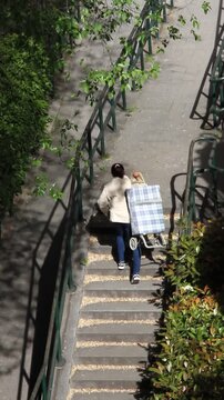 Mujer subiendo carro pesado de la compra a pulso coja por escaleras con carrito de comida lleno a hombros cargando peso del supermercado por pelda&ntilde;os 