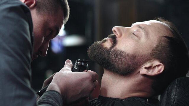 Skilled barber grooming client's beard using electric razor, delivering precise styling within contemporary barbershop setting