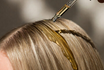 Fototapeta premium A dropper is applying hair oil to a person’s scalp. It appears to be a bathroom setting.