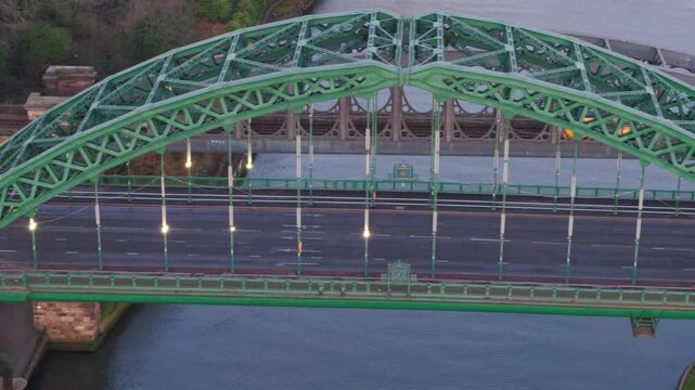 Aerial telephoto tracking shot moving sideways alongside the Wearmouth Bridge in Sunderland at dawn, featuring early morning traffic and the Monkwearmouth Railway Bridge in the background.