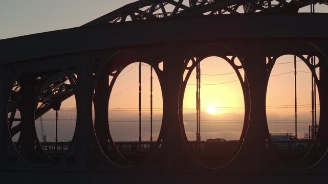 Aerial telephoto tracking shot of the Wearmouth and Monkwearmouth Railway Bridges silhouetted against a vibrant sunrise in Sunderland, with early morning traffic crossing