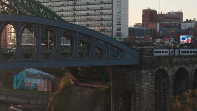 Static aerial telephoto shot of a Northern Rail passenger train crossing the Monkwearmouth Railway Bridge into Sunderland city center at dawn.