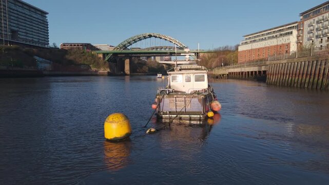 Low-altitude aerial drone shot tracking around a small blue boat moored on the River Wear, revealing the Wearmouth Bridge and Monkwearmouth Railway Bridge in Sunderland.