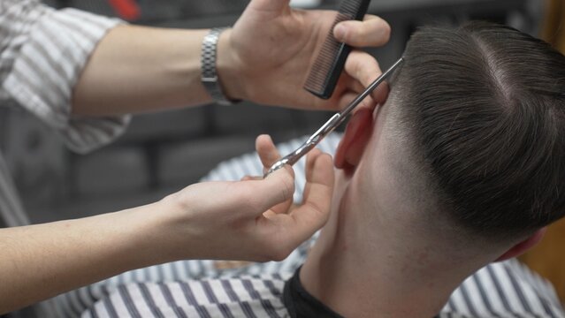Professional barber cutting client's hair with scissors and comb, creating a stylish fade in a modern barbershop, providing a high quality grooming service