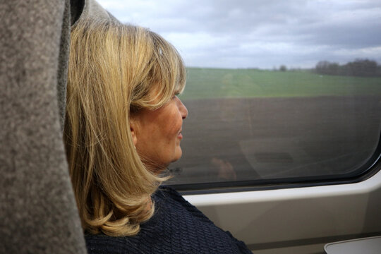 Donna bionda di profilo seduta sul treno che guarda fuori dal finestrino il paesaggio di campagna scorrere durante un viaggio