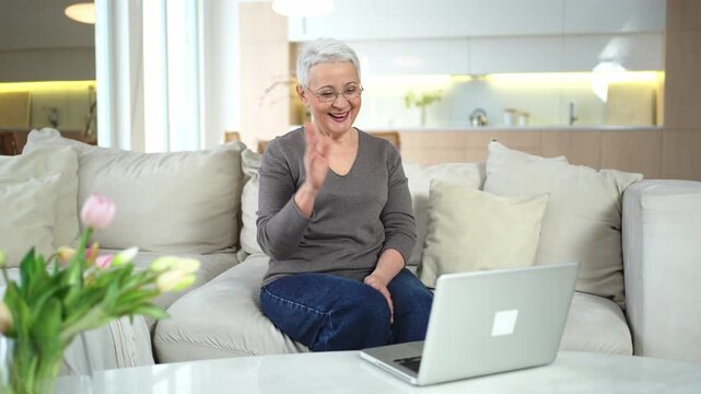 Happy middle aged senior woman siting with laptop talking on video call with friends family. Laughing mature old senior grandmother having fun talking speaking with grown up children online