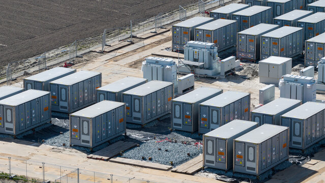 Aerial view of a large battery energy storage system with rows of grey container units and electrical transformers on a gravel site in Espel, Flevoland, Netherlands.