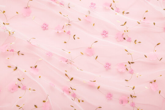 New transparent soft wrinkled tulle fabric with flower pattern on light pink table background. Pastel color. Closeup. Top down view.