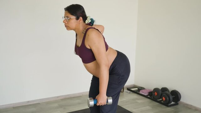 Pregnant Indian female exercising shoulders with weights during third trimester of pregnancy