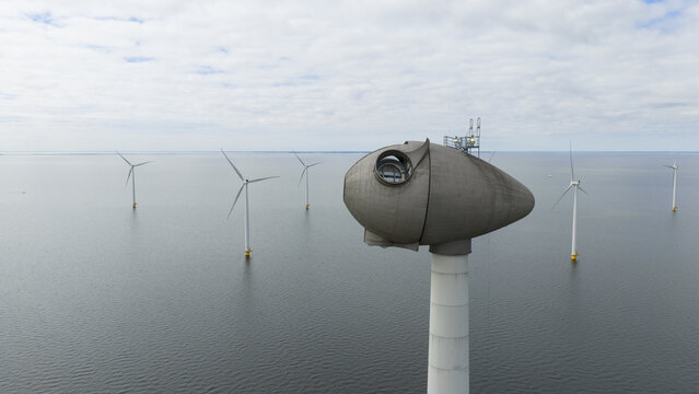 Aerial view of the Westermeerdijk wind turbine nacelle and offshore wind farm over calm sea water under a cloudy sky in Espel, Flevoland, Netherlands.