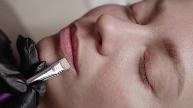 Procedure microblading, portrait of woman applying permanent tattoo makeup on lips in beauty salon.