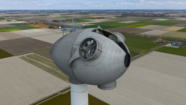 Aerial view of the nacelle of a large wind turbine overlooking vast agricultural fields and flat polder landscape under a cloudy sky Espel, Flevoland, Netherlands.