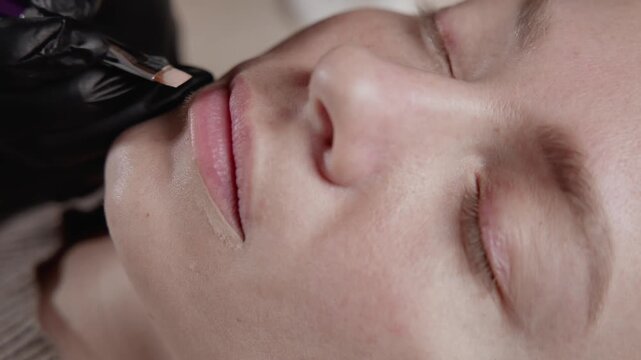 Portrait of woman applying permanent tattoo makeup on lips in beauty salon, Procedure microblading.
