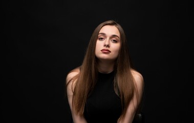 Fototapeta premium Young woman with long brown hair posing for an elegant portrait, looking directly at the camera with a confident expression