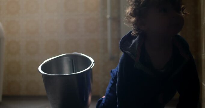 Baby sitting on kitchen floor staring at metal container before slowly crawling away, curious gaze and gradual movement showing exploration, attention shift and natural discovery
