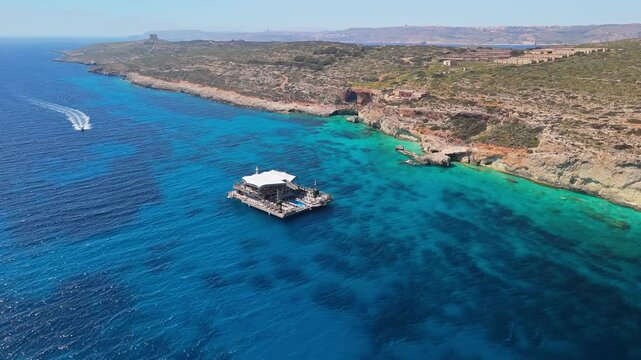 Noma Island, a floating venue anchored off the coast of Comino in Malta&rsquo;s Mediterranean archipelago, features an outdoor lounge, bar, and pool, captured in an orbital bird&rsquo;s-eye view.