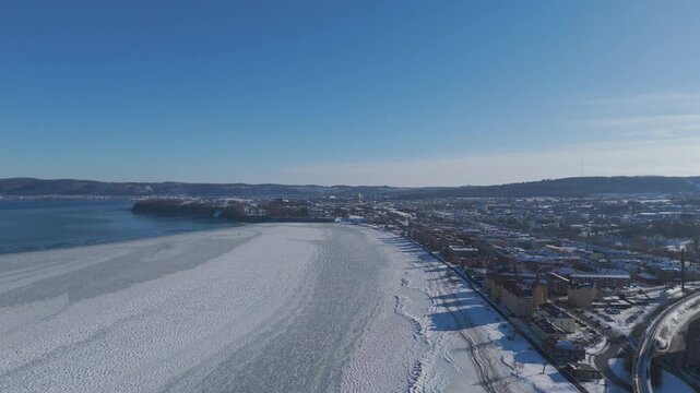 Aerial drone view of Oulu Finland featuring frozen coastline, snow covered cityscape and waterfront under clear blue sky, wide winter landscape with urban setting