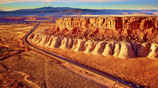 Drone shot drifting away from a sandstone mesa as sunset colors light up the rugged cliffside