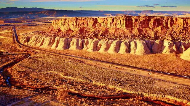Cinematic drone pullback from red rock plateau showcasing a glowing sunset-washed rock face