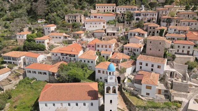 Aerial panoramic view historic hillside village of Dhermi in Albania. Traditional orange rooftop stone houses and iconic Holy Church of Saint Spyridon