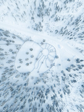 Aerial view of a traditional reindeer corral surrounded by a dense pine forest covered in deep snow in Lapland, Finland.