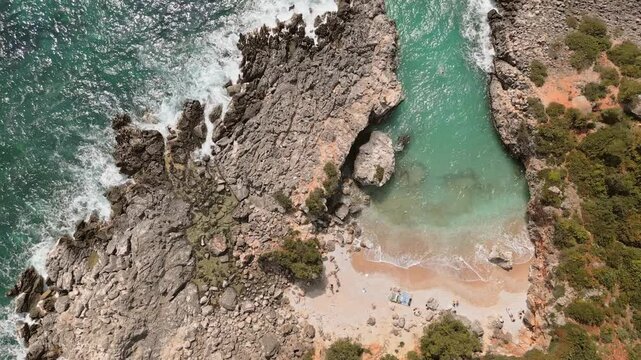 Aerial view isolated Aquarium Bay beach in Albania with tourist sunbath. Hidden paradise with crystal clear turquoise water for swimming,snorkeling, relaxation. Secluded rocky cove on Albanian Riviera