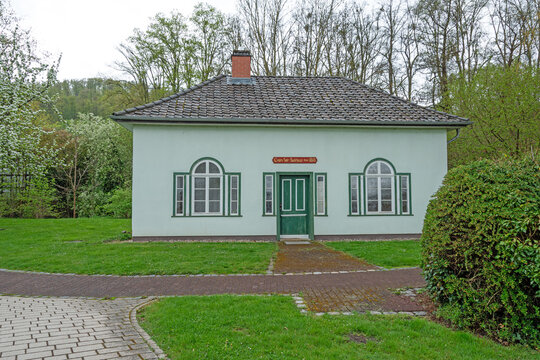 Front view of a historic brine bathhouse from 1818 with symmetrical facade and calm park surroundings.
