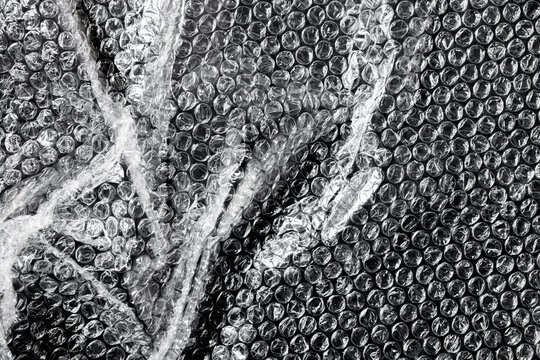 Transparent plastic bubble wrap with wrinkled overlay effects. Glossy film texture with realistic light reflections for creative industrial design.