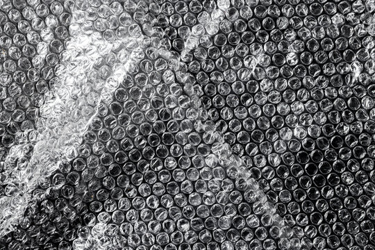 Transparent plastic bubble wrap with wrinkled overlay effects. Glossy film texture with realistic light reflections for creative industrial design.