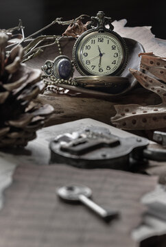 A collection of aged curiosities rests in a tableau of quiet nostalgia, bathed in ethereal light. At the center, a classic pocket watch perches on weathered wood, its hands frozen against an ivory fac