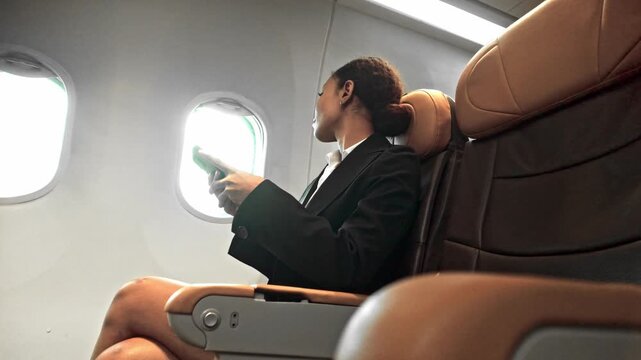 Passenger in business attire sits by an airplane window, reading a document in a modern cabin with tan leather seats.